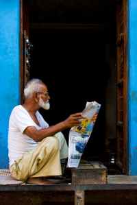 old man sitting while holding newspaper article